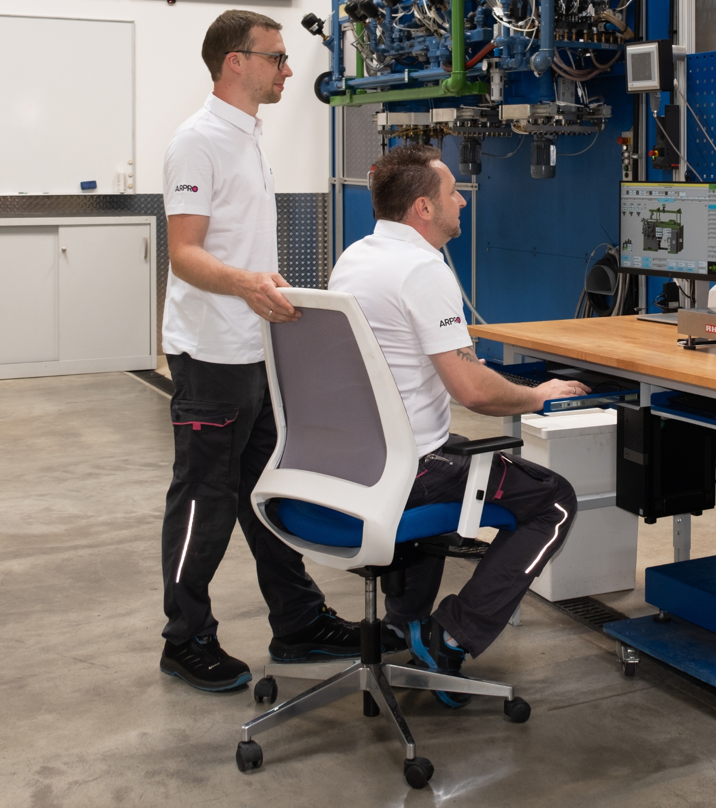Two gentleman sitting at a computer wearing white ARPRO polo shirts