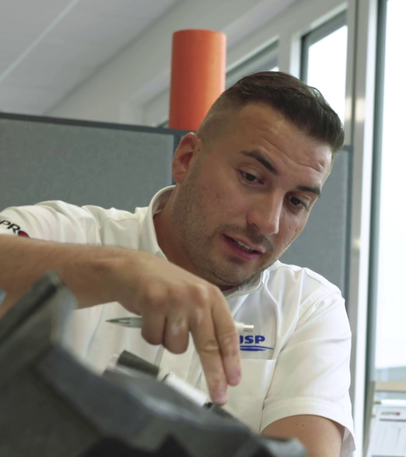 A man wearing a white JSP polo shirt pointing to an ARPRO part