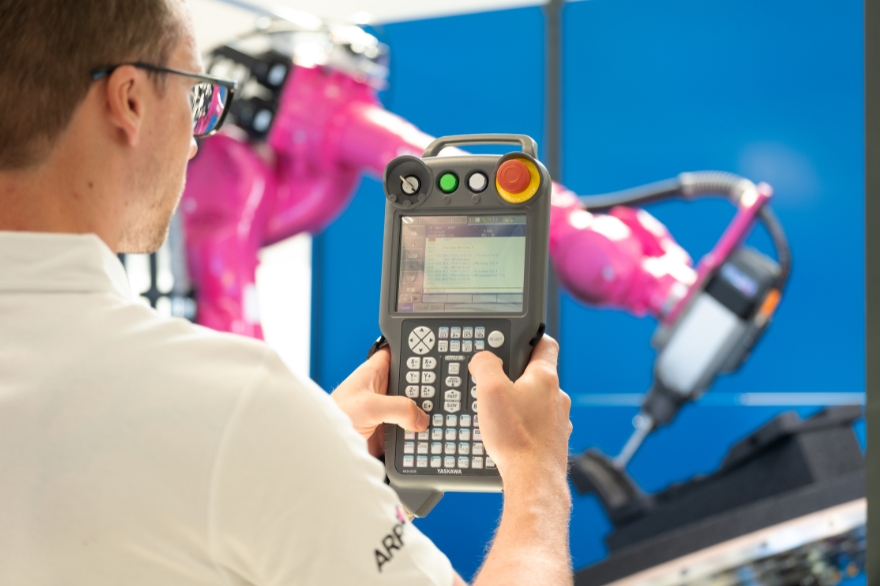 Man in foreground holding control for the magenta 8-axis robotic milling system in the background.
