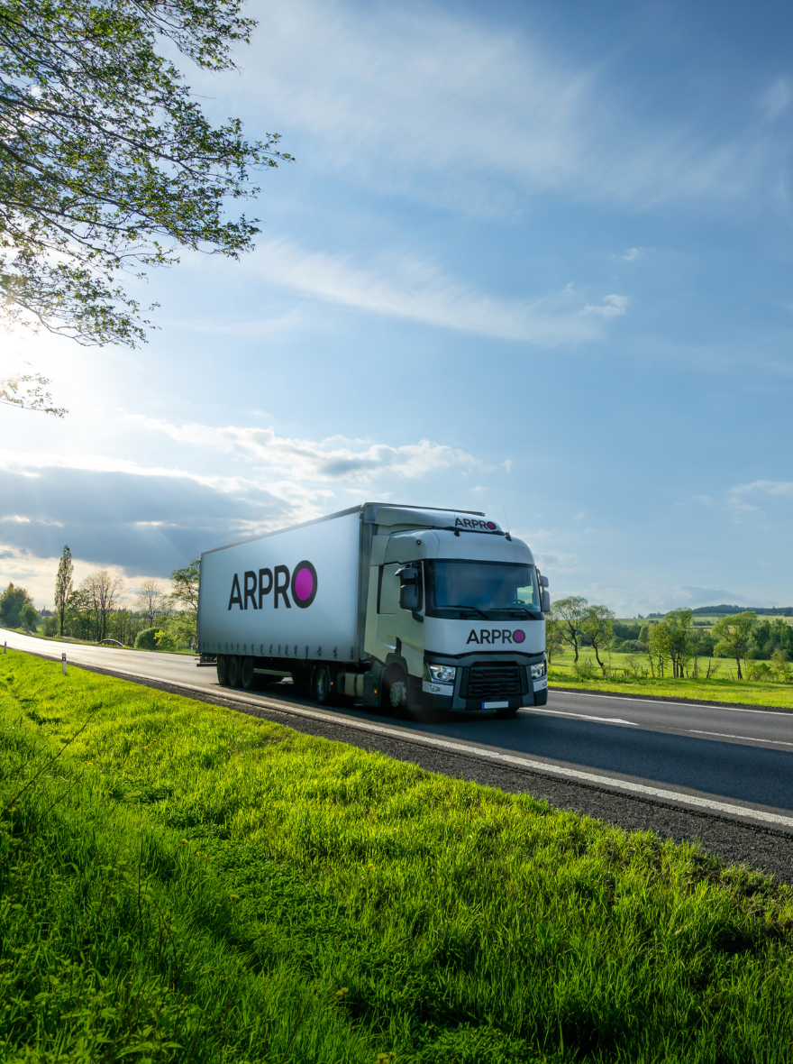 Bílý nákladní vůz s logem ARPRO projíždí zelenou krajinou