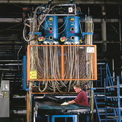 Factory based image showing a person working at a large steam chest machine producing ARPRO parts. Lots of blue, orange and grey machine parts of pipe work. 
